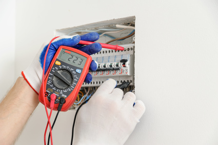 Electrician check voltage in electrical fuse box with a multimeter.
